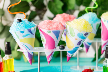Flavoured snow cones with crazy straws in a stand against a blurred background.