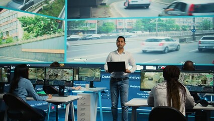 Indian team leader overseeing his employees work on surveillance footage observation, ensuring...