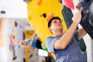 Male alpinist practicing indoor rock-climbing on artificial boulder without safety belts