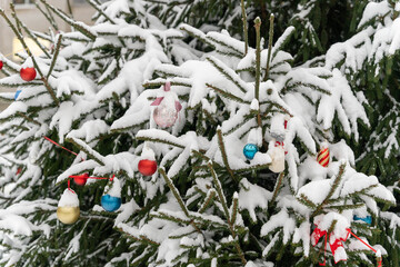 A Christmas tree adorned with colorful ornaments, covered in snow.