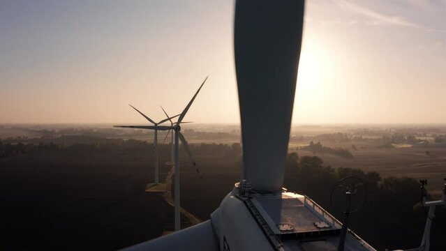 Aerial view of wind turbines standing in a field at sunrise. Their sleek blades slowly turning, catching the first rays of sunlight as they rise over the horizon.