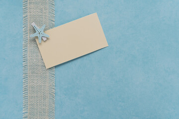 soft blue textured background with natural white burlap ribbon border and off white blank card held...