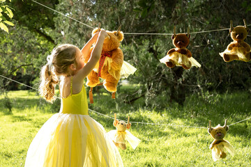 Girl in yellow lifting teddy bear from clothesline.