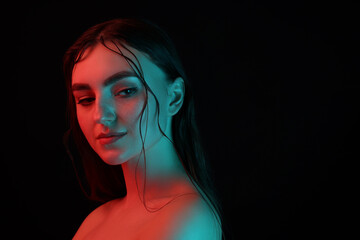 Fototapeta premium Portrait of beautiful woman in neon lights against black background. Space for text