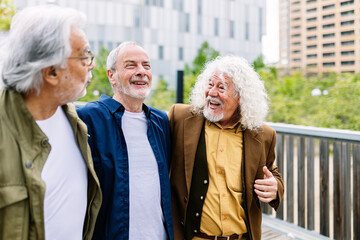 Happy senior men having fun together walking outdoors. Three older male friends laughing while...