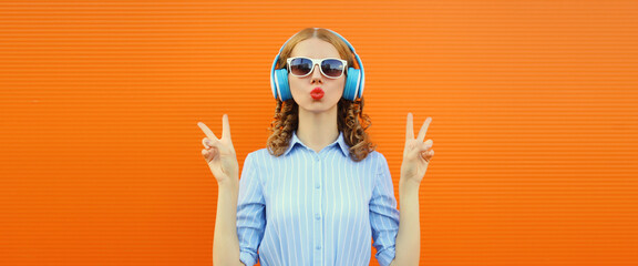 Happy modern happy young woman listening to music with headphones on bright orange background