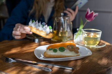 A woman in a blue shirt enjoys a pastry and tea at a wooden table in a cafe, with a tulip in the...