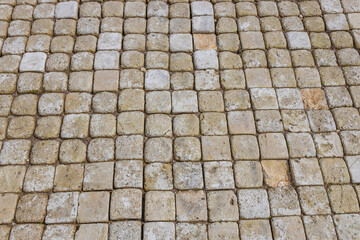  A close-up view of an outdoor stone pavement featuring a grid pattern of aged, weathered stones with varying shades of beige and grey, showcasing the beauty of natural stone craftsmanship...