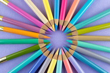 Fototapeta premium Colorful wooden crayons arranged in a circle on a purple paper background