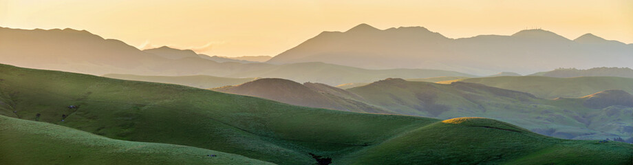 Panorama of mountains at sunrise, sunset, with green pasture, grass