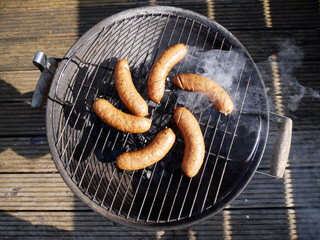 Country sausages on the grill grate in subtle smoke.
A summer day on the terrace.  