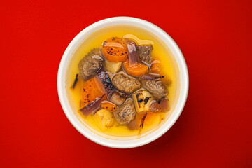 Beef stew with broth, soup with meat and vegetable on red background, top view