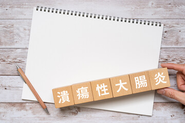 潰瘍性大腸炎と書かれたブロック、ノート、手
