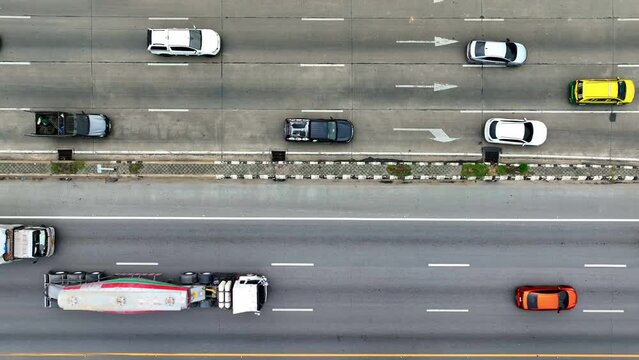 From above, witness a bustling multi-lane thoroughfare with cars, a motorbike, and a towering truck, each confined within crisp lane dividers, epitomizing the dynamic pulse of transportation.
