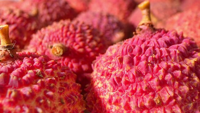 Explore the tantalizing charm of lychees through a close-up lens, revealing their rough, crimson skin with unparalleled clarity. Experience the sensory delight of this exotic fruit. 
