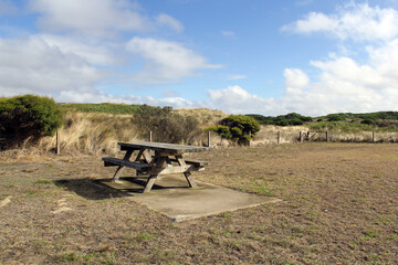 Picnic table in a natural landscape with grass and hills under a blue sky at Killarney Beach near Port Fairy in Victoria, Australia