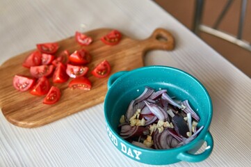 Lettuce in the process of cooking, red onion and garlic are in a bowl, tomatoes on a wooden board in the background, cut into pieces