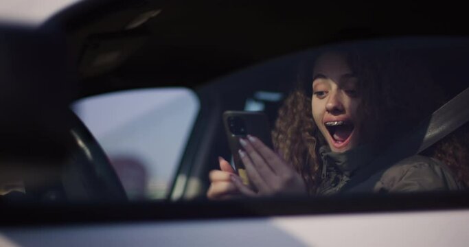 Teenage girl with curly hair and braces captures a selfie in her car, playfully sticking out her tongue and flashing a peace sign.