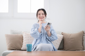 Young woman thinking with her phone in a beautiful living room, looking at the screen, smiling and finding something to do, front, looking at the camera.