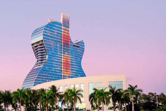 Guitar shaped architecture facade of the Hard Rock Hotel (Oasis Tower) with palm trees and purple sunset in Florida, United States