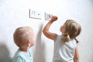 Little children playing with electrical socket indoors. Dangerous situation