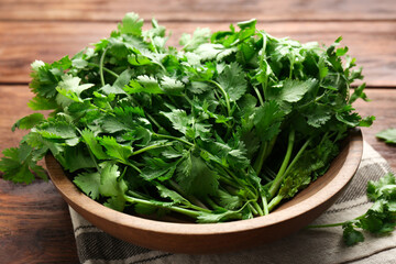 Fresh coriander in bowl on wooden table, closeup