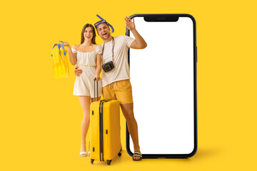 Beautiful young happy couple of tourists with suitcase, flippers and snorkeling mask on yellow background