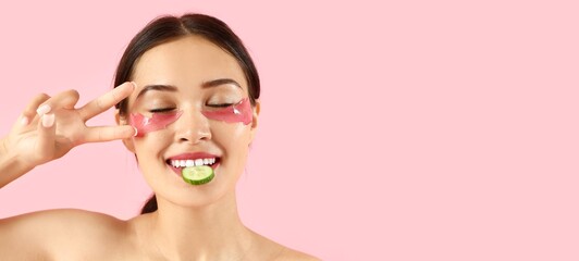 Pretty young woman with under-eye patches and cucumber slice on pink background with space for text