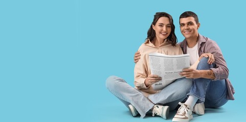 Young couple reading newspaper while sitting on blue background with space for text