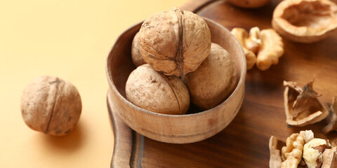 Bowl of tasty walnuts on yellow background