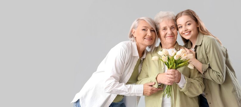Young woman with her mother and grandma holding tulips on grey background with space for text - Powered by Adobe