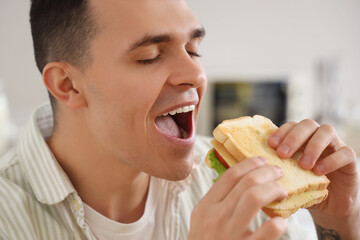 Young man eating tasty sandwich made from toasts in kitchen, closeup
