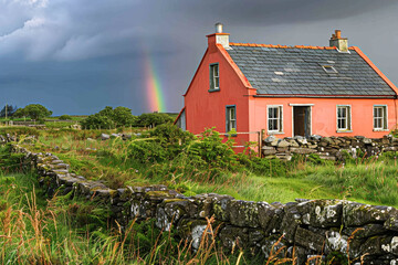 A coral-colored house with a slate roof in a lush Irish meadow, with ancient stone walls and a distant rainbow.