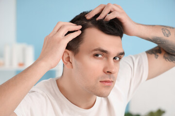 Young man with hair loss problem in bathroom, closeup