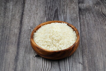 Raw white rice on black background. Long uncooked rice in wooden plate. Natural organic food. Traditional Asian cereal culture.