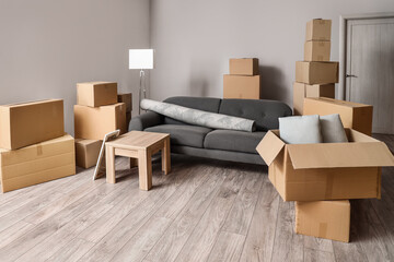 Cardboard boxes with black sofa, rolled carpet and table in living room on moving day