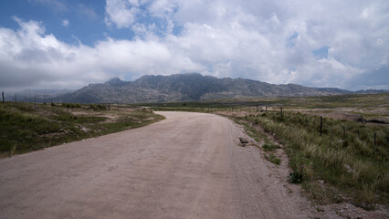 View of the dirt road across the green field and hills, leading to the rock massif The Giants in Cordoba, Argentina.