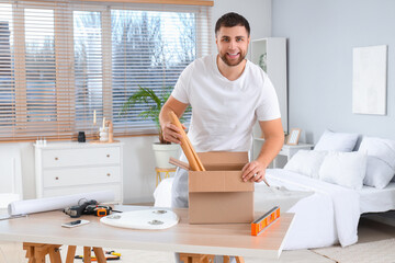 Young man taking table legs from box for assembling in bedroom