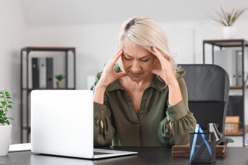 Mature businesswoman experiencing menopause at table in office