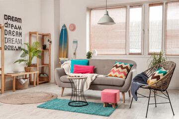 Interior of stylish living room with shelving unit, surfboard and grey sofa