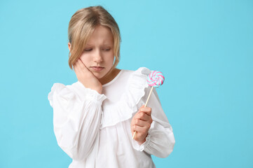 Young girl holding lollipop and suffering from toothache on blue background