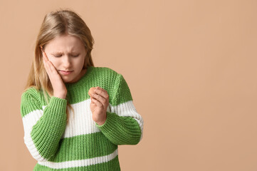 Young girl holding cookie and suffering from toothache on beige background