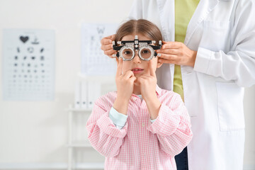 Female ophthalmologist putting trial frame on little girl in clinic