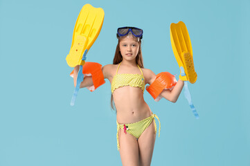 Cute little happy girl in swimsuit with inflatable armbands, flippers and snorkeling mask on blue...