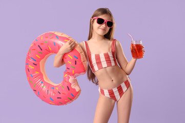 Cute little happy girl in swimsuit with inflatable ring and glass of lemonade on purple background