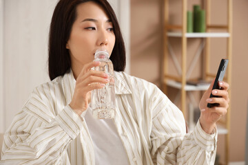 Young Asian woman with mobile phone drinking water in office, closeup