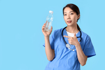 Female Asian doctor pointing at bottle of water on blue background