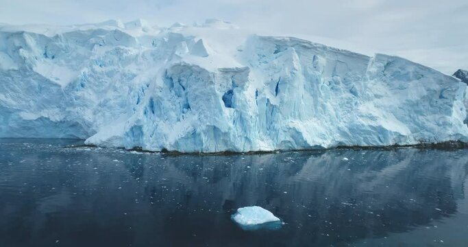 Beautiful towering huge iceberg floating tranquil cold Antarctica ocean. Snow covered blue ice wall glacier reflecting calm water. Ecology, melting ice, climate change and global warming concept