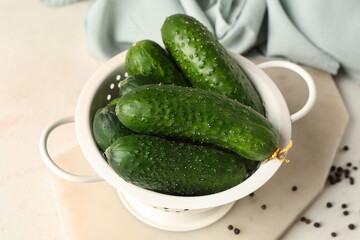 Colander with fresh green cucumbers and peppercorn on white background