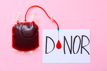 Blood pack and paper sheet with text DONOR on pink background. World Blood Donor Day